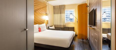 Habitación de hotel con cama, escritorio, televisor y ventana con vista a la ciudad.