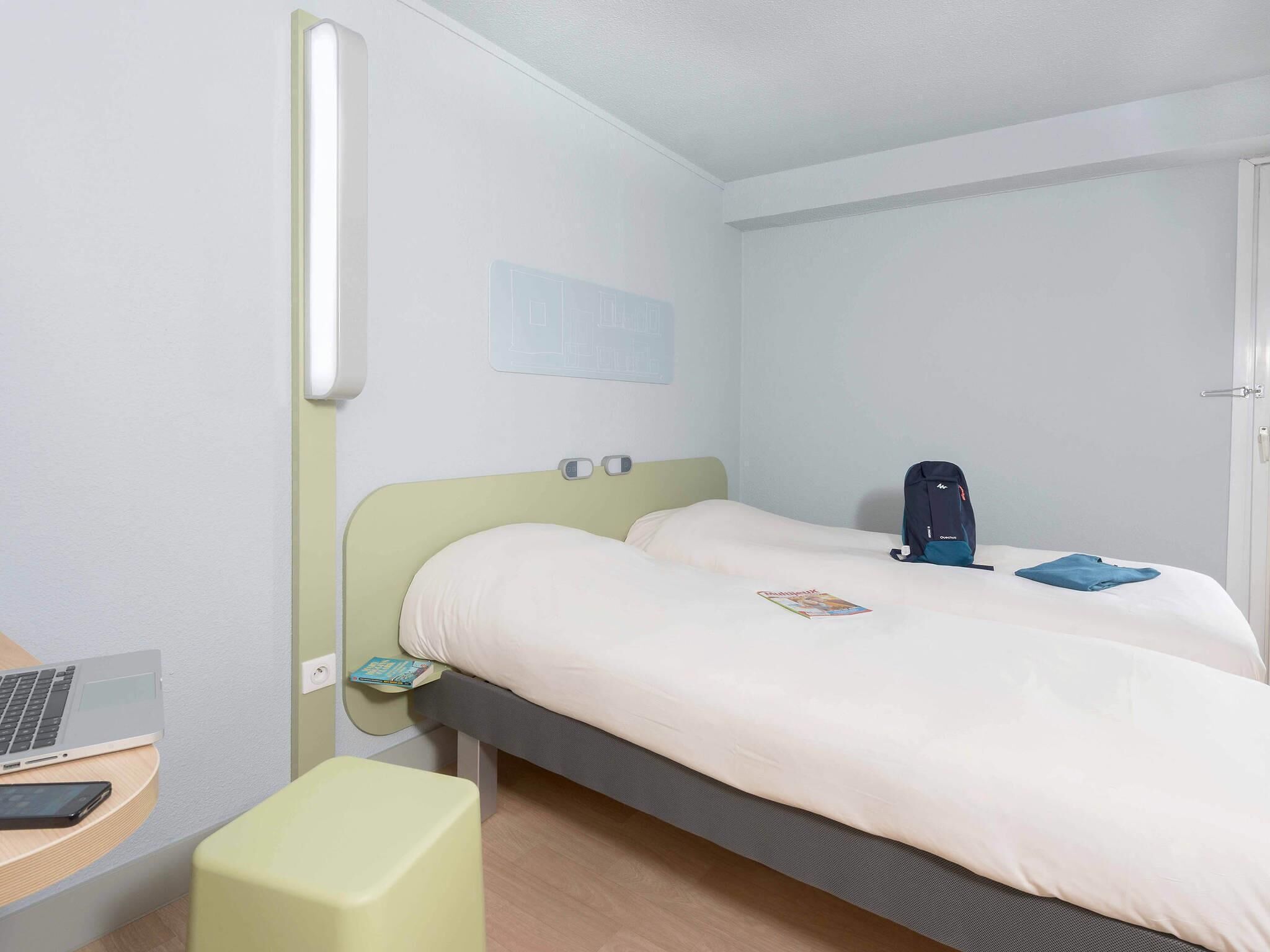 Une chambre d’hôtel avec un lit, un bureau avec un ordinateur portable, une chaise et une table de chevet avec un livre.