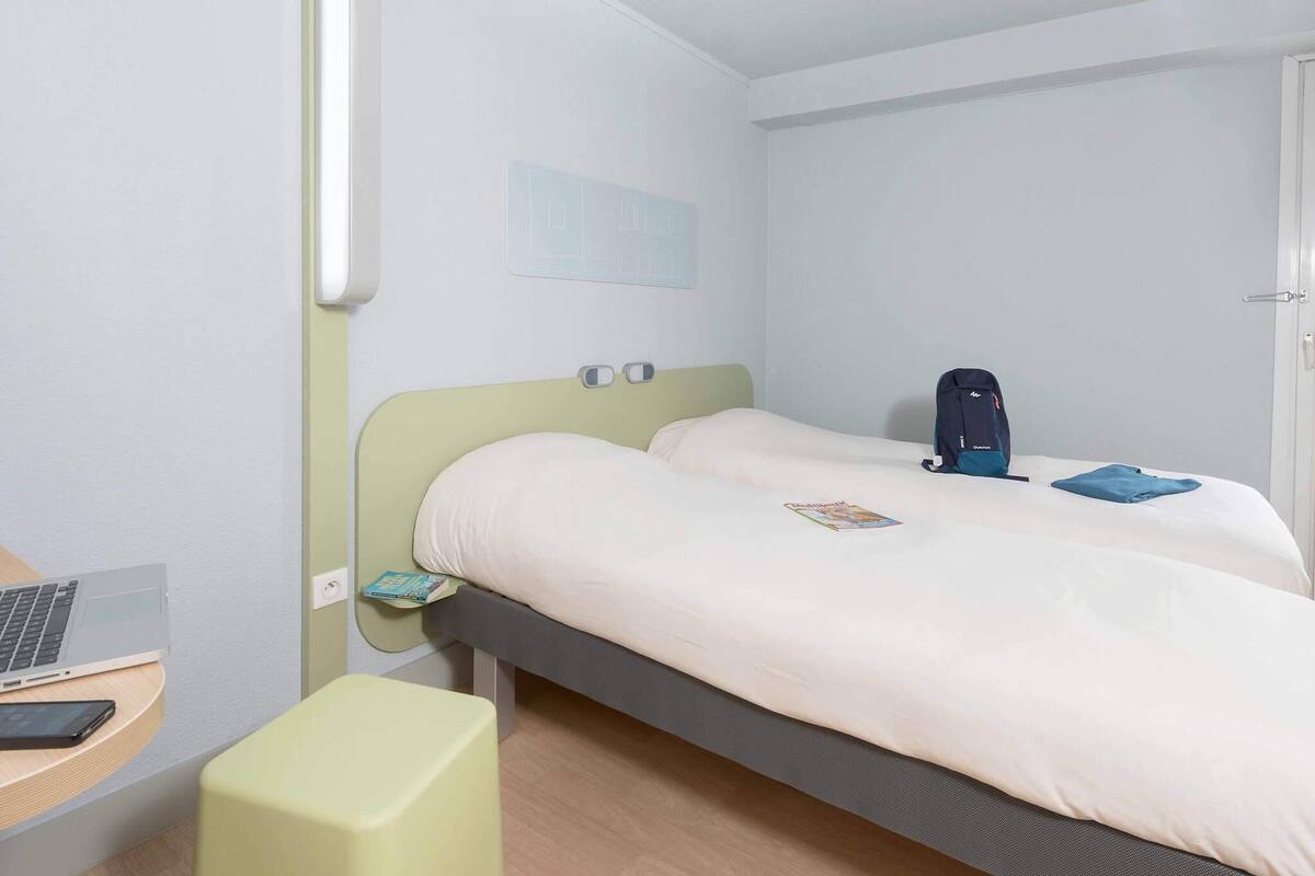 Une chambre d’hôtel avec un lit, un bureau avec un ordinateur portable, une chaise et une table de chevet avec un livre.