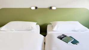 Une chambre d’hôtel avec deux lits, chacun doté de draps et d’oreillers blancs. Un luminaire mural est fixé au-dessus des lits, et un panneau décoratif vert, orné de motifs évoquant l’herbe, agrémente le mur.