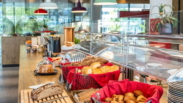 Zona de bufé con panes y pasteles diversos expuestos en cestas y una tabla de cortar.
