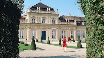 A large, classical building with symmetrical architecture, a central entrance, and a formal garden with trimmed hedges.