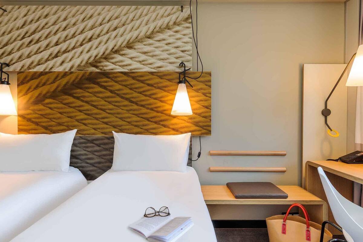 Une chambre d’hôtel comprenant un lit, des tables de chevet, un bureau, une chaise et un mur orné d’un motif géométrique.