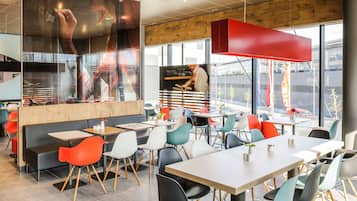 Ein modernes Restaurant-Interieur mit verschiedenen Sitzmöglichkeiten, darunter Sitzecken und Tische, und einem großen Fenster mit Blick auf die Straße.