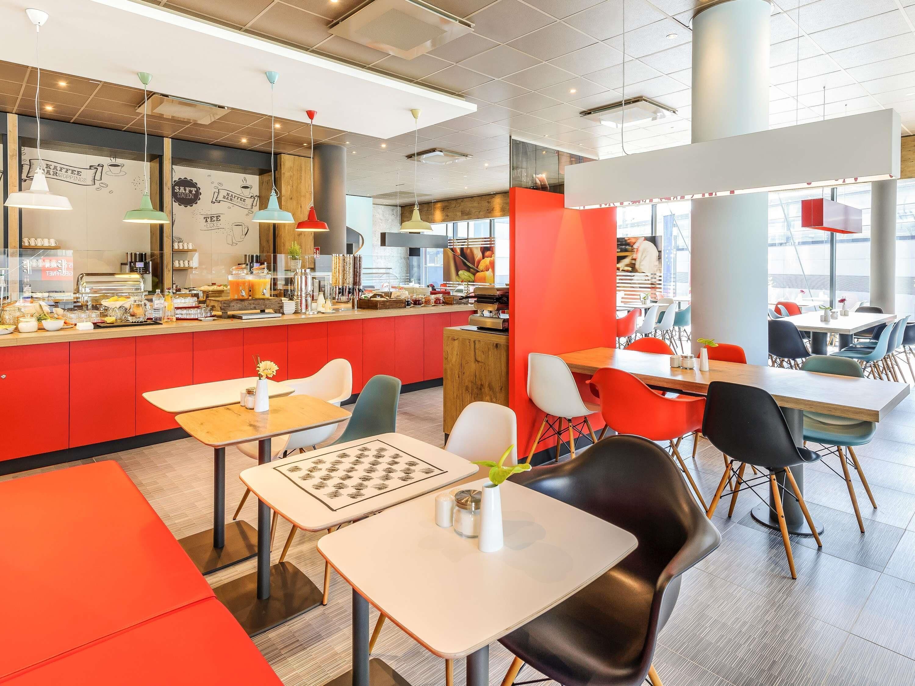 A modern cafe with red and white decor, multiple seating areas, and a visible kitchen area.