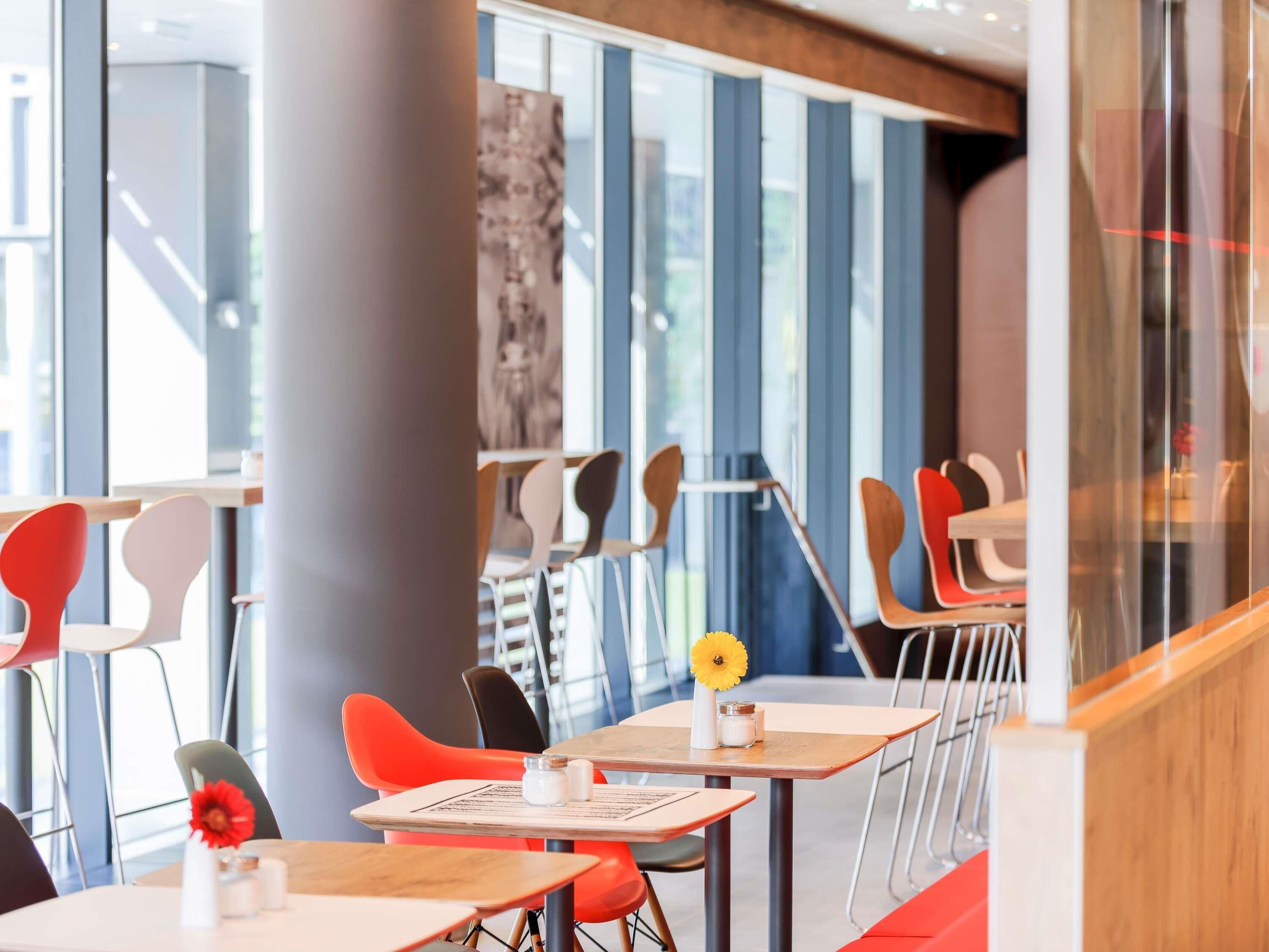 A modern dining area with high tables and chairs, large windows, and a stone pillar.