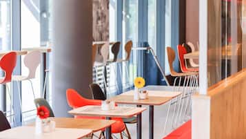 A modern dining area with high tables and chairs, large windows, and a stone pillar.