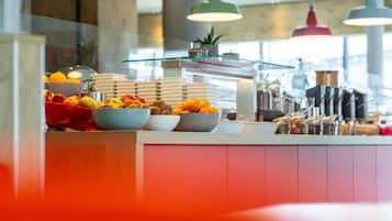 Un bufé de desayuno con diversas frutas y fuentes de comida, un expositor de vidrio y lámparas colgantes.
