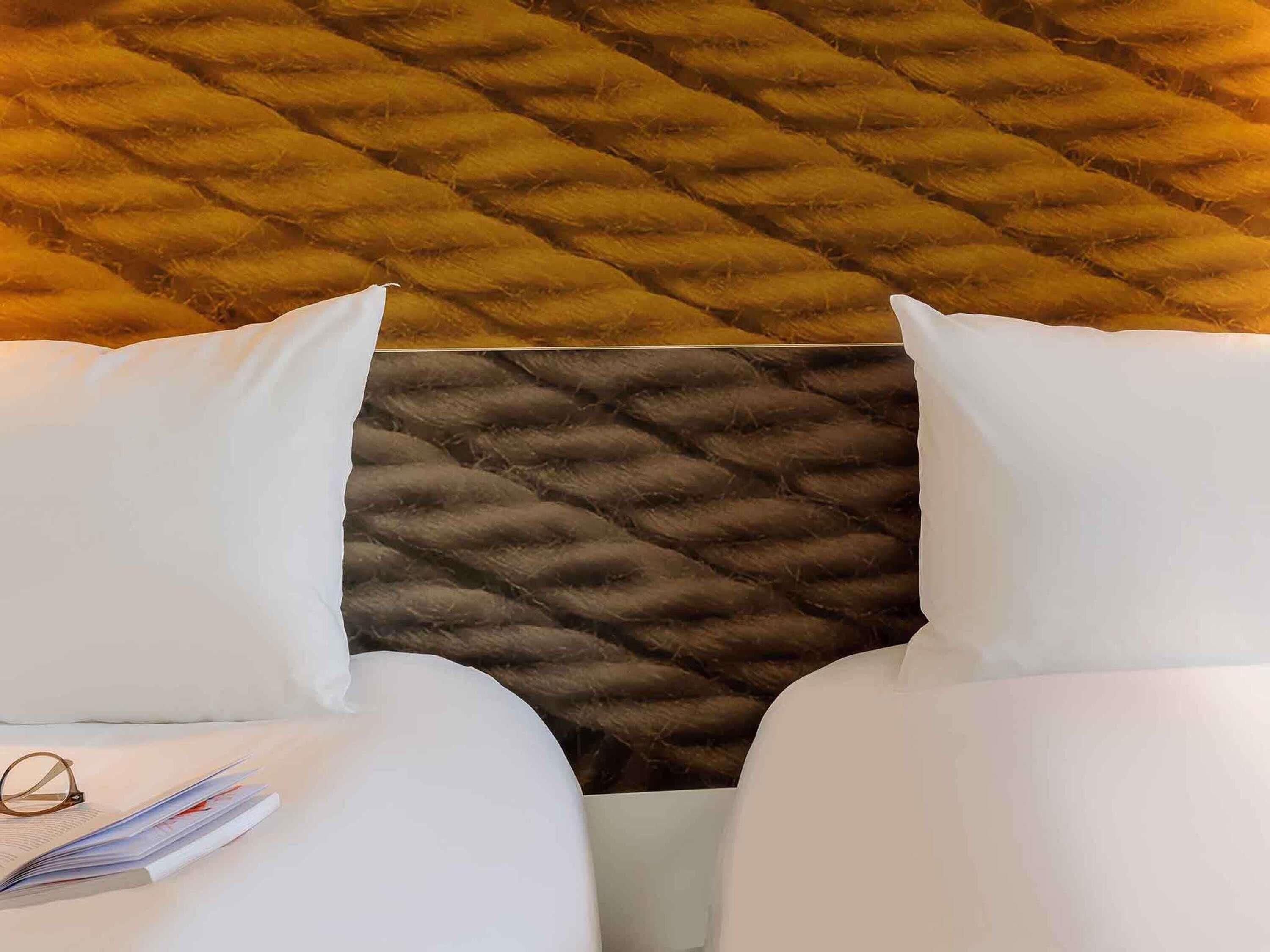 A bed with a tufted headboard, white bedding, and a pair of glasses on the pillow.