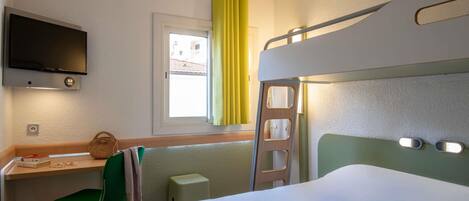Quarto de hotel com uma cama beliche, uma escrivaninha com cadeira, televisão fixada na parede e janela com cortinas amarelas.