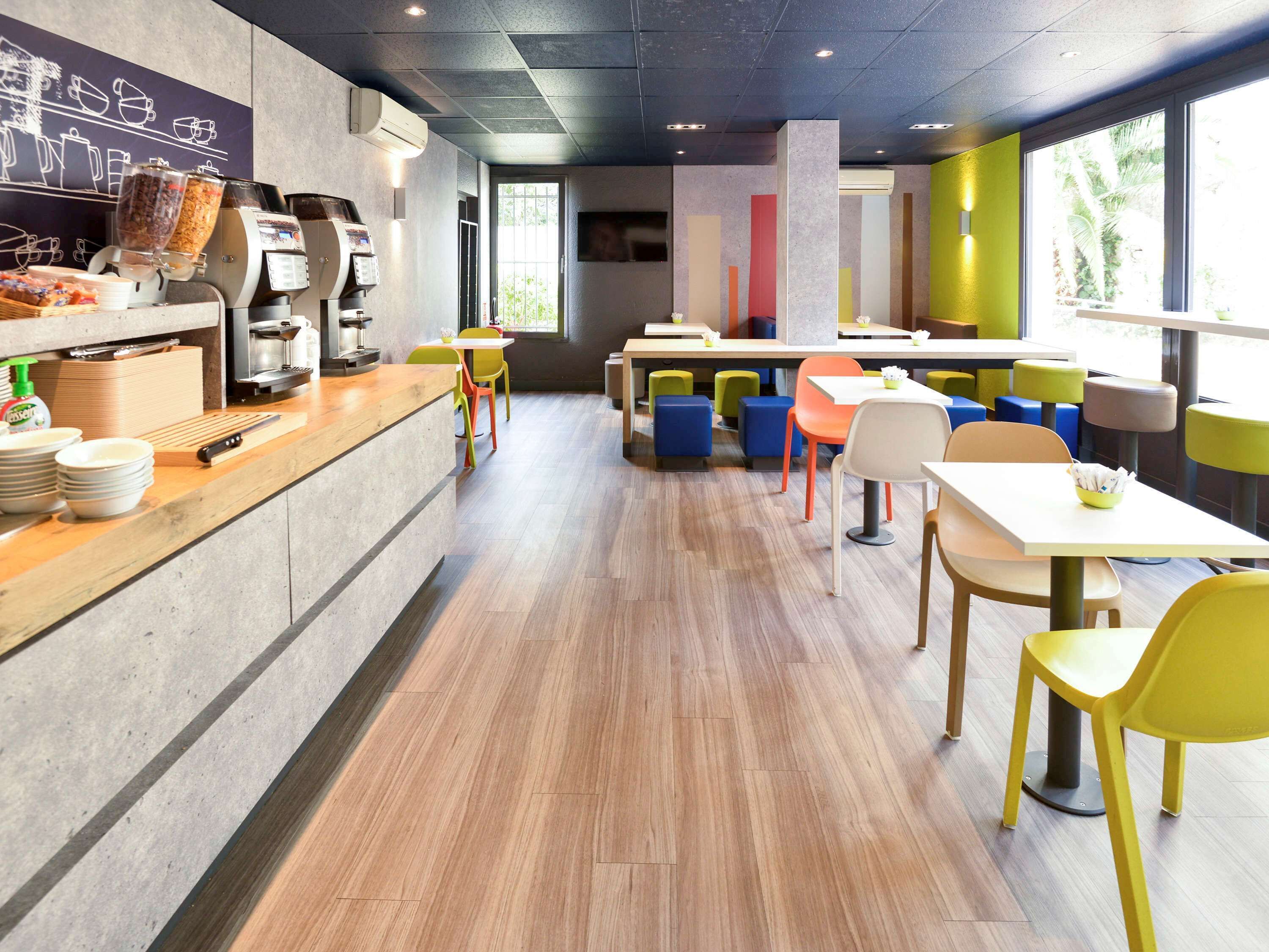 Una cafeteria moderna amb una màquina de cafè, zona de seients i vistes a vegetació a l'exterior.