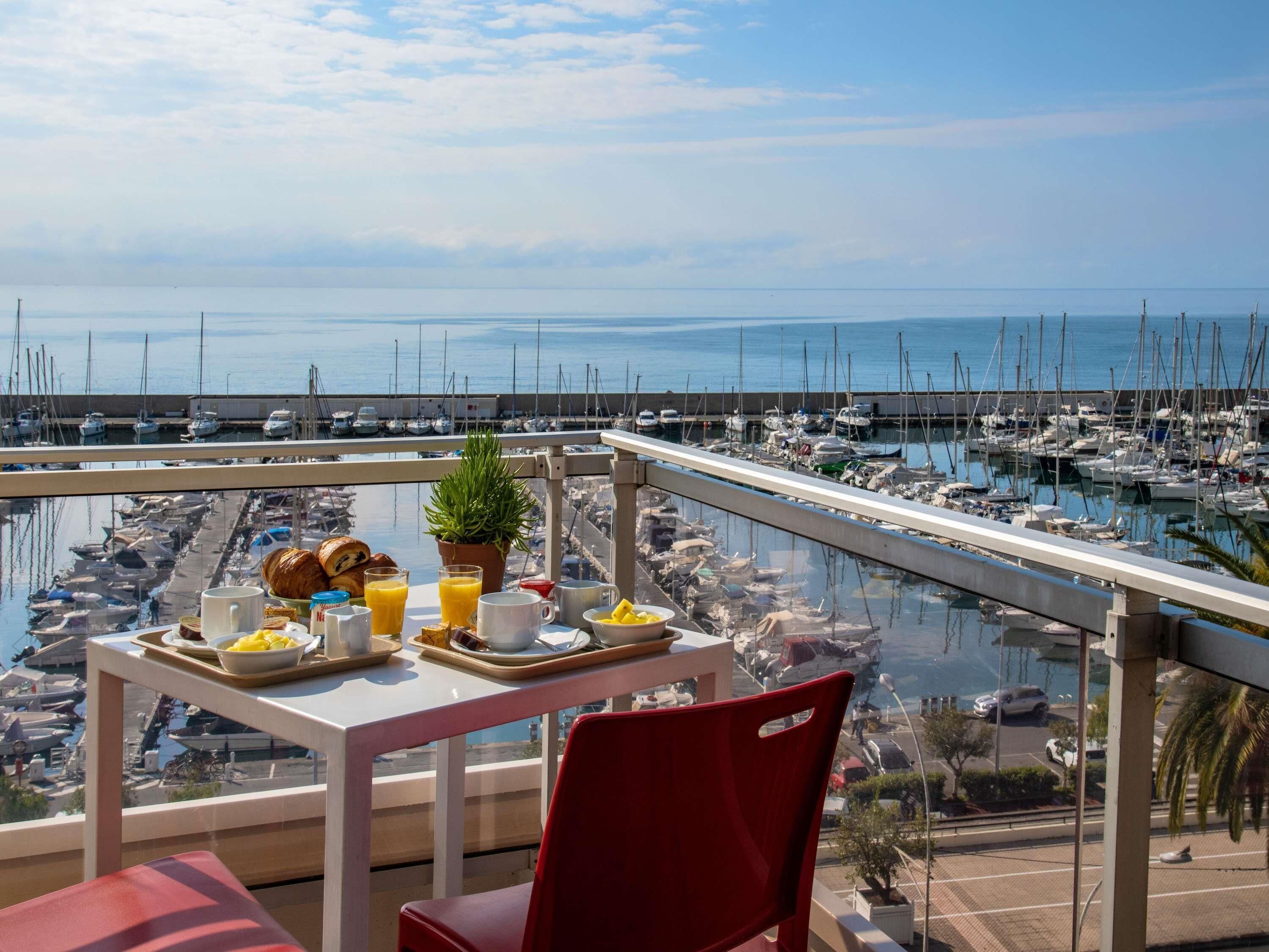 Un balcón con mesa dispuesta para el desayuno, con vistas a un puerto deportivo y barcos.