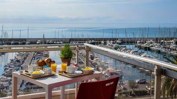 Un balcón con mesa dispuesta para el desayuno, con vistas a un puerto deportivo y barcos.