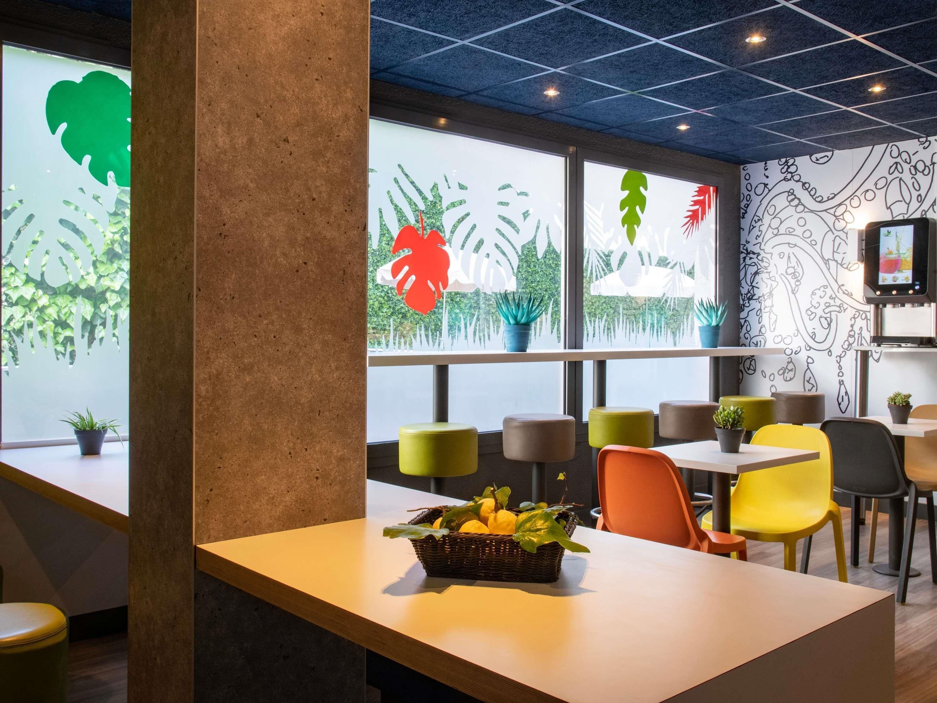 Un interior de restaurante moderno con una barra central, sillas coloridas y motivos vegetales decorativos en las paredes.