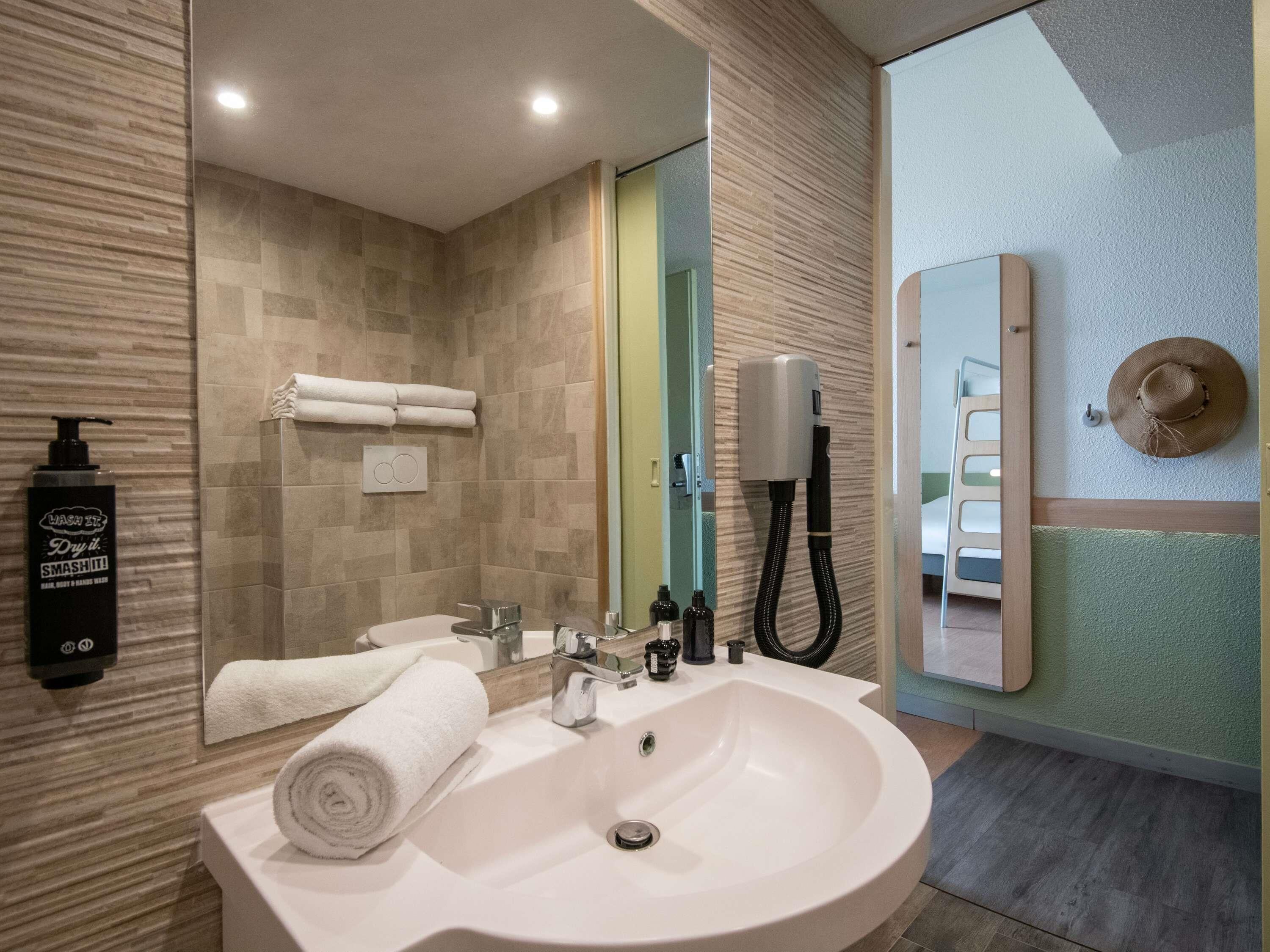A modern bathroom with a large sink, a mirror, a towel rack, and a shower area.