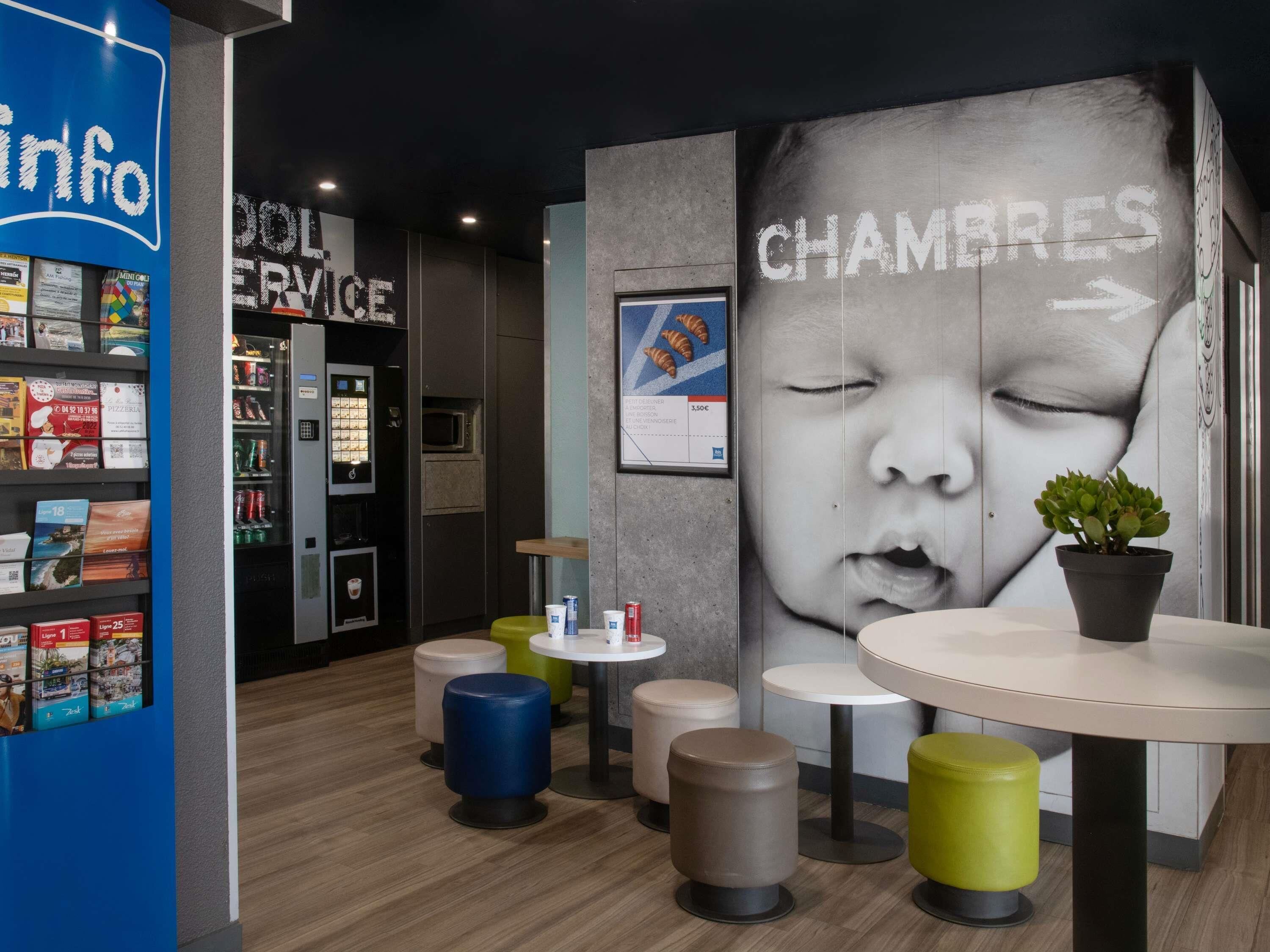 Un intérieur moderne agrémenté d’une grande fresque murale, d’un distributeur automatique et d’un petit espace détente avec des tabourets.