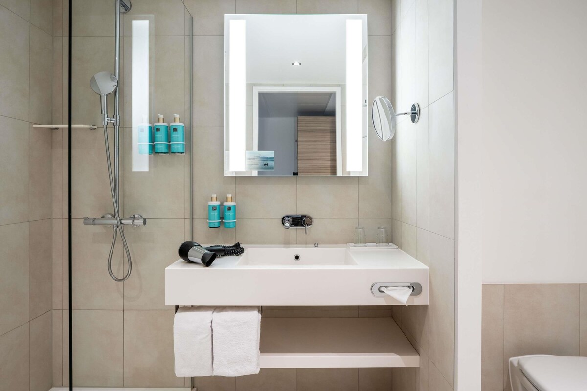 A modern bathroom with a glass-enclosed shower, a white sink, and a mirror above it.