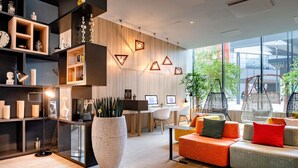 Un interior moderno con una planta grande en maceta, un sofá con cojines de colores y un escritorio con dos computadoras.