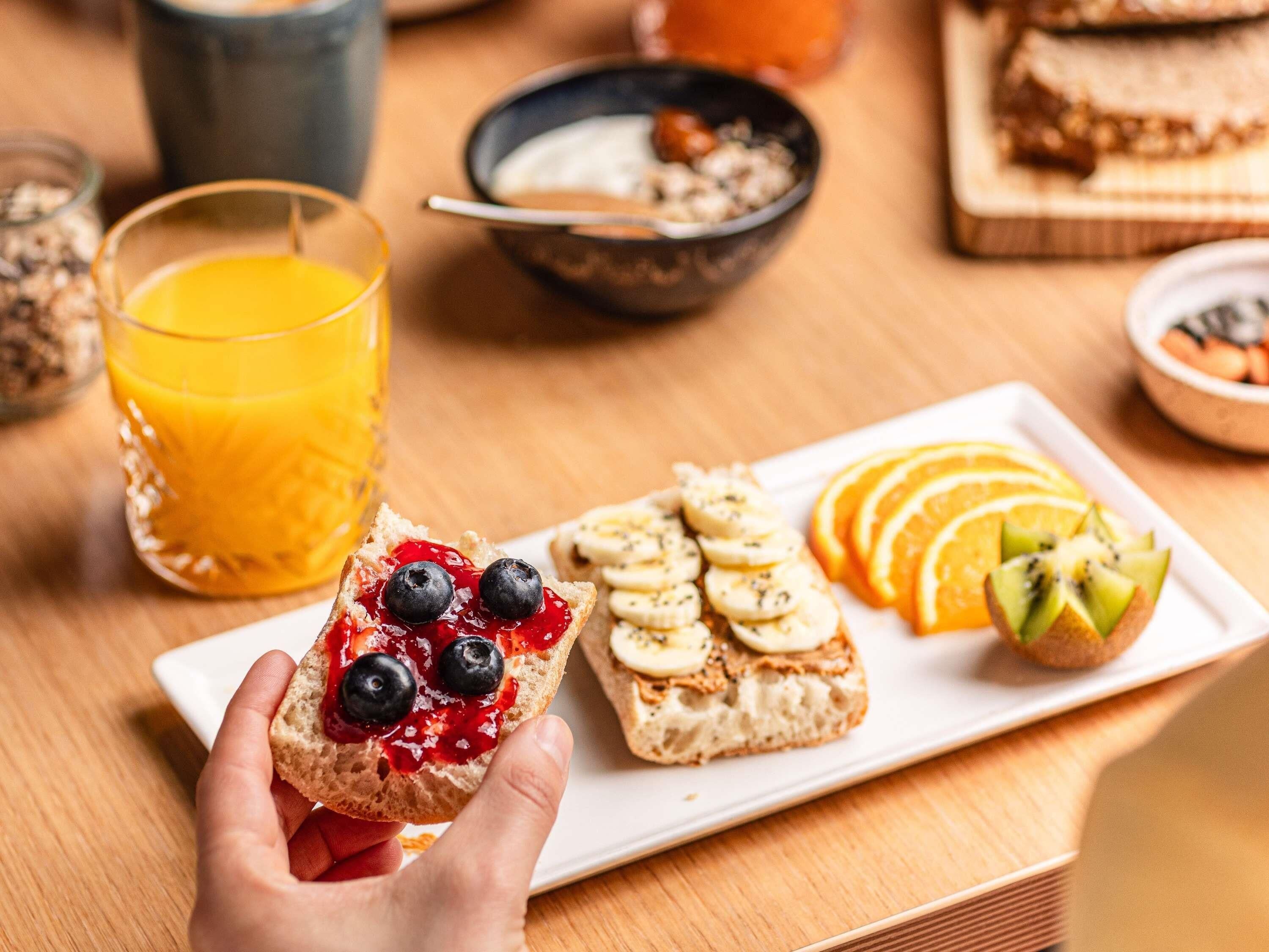 Uma mesa de café da manhã com torradas, frutas e um copo de suco de laranja.
