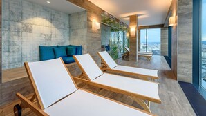Un spa moderno con sillones de descanso, una camilla de masaje y un amplio ventanal con vistas a la ciudad.