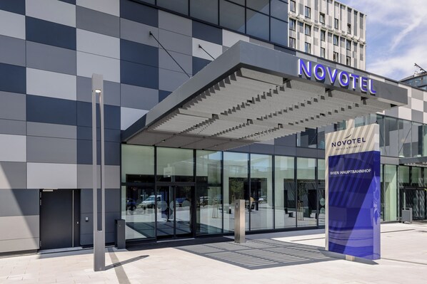 Una entrada de hotel moderna con fachada de vidrio y un llamativo letrero 'NOVOTEL'.