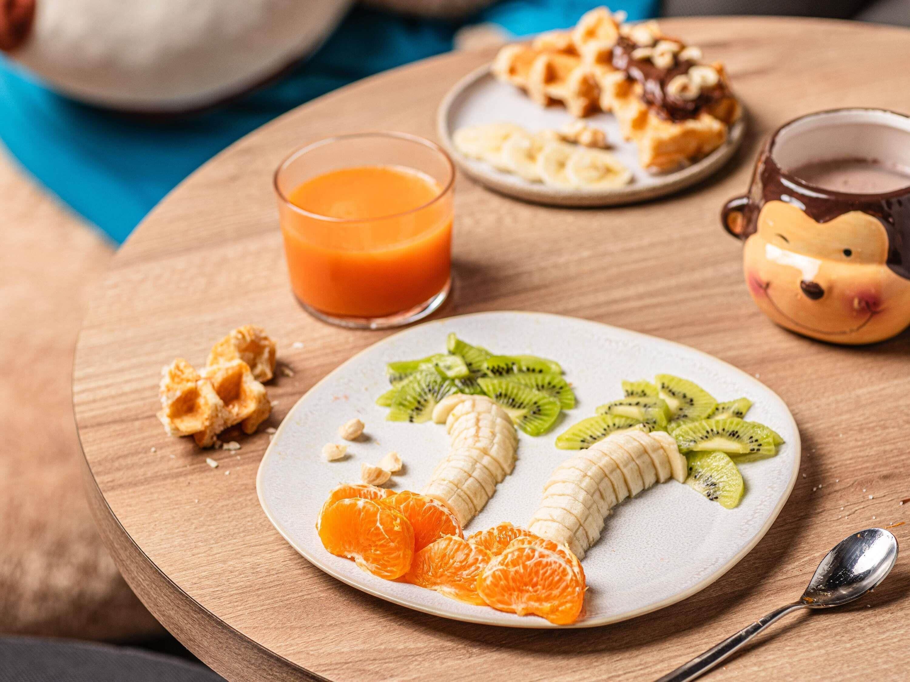 Desayuno con una fuente de fruta, un vaso de zumo de naranja y una taza sobre una mesa de madera.