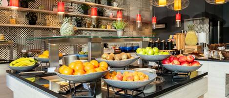 A buffet with various fruits and vegetables, a modern kitchen area, and hanging pendant lights.