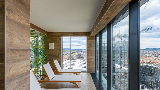 Un área de descanso moderna con paneles de madera y ventanas amplias que ofrecen vista a la ciudad.