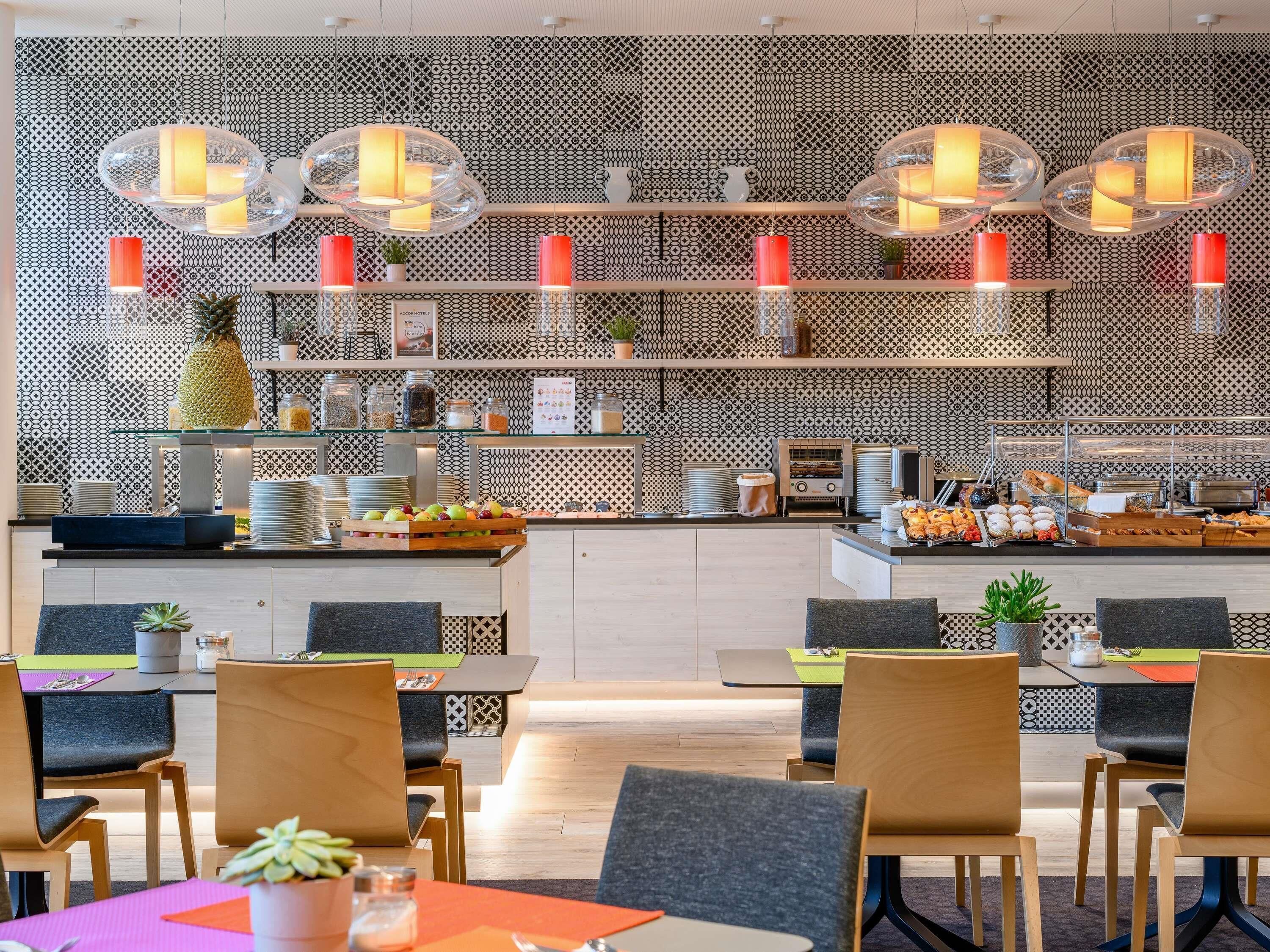 A modern dining area with a patterned wall, clear glass pendant lights, and a buffet counter with various food items.