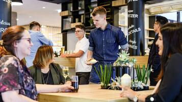 Uma área de bar moderna, com assentos e um barman servindo bebidas.