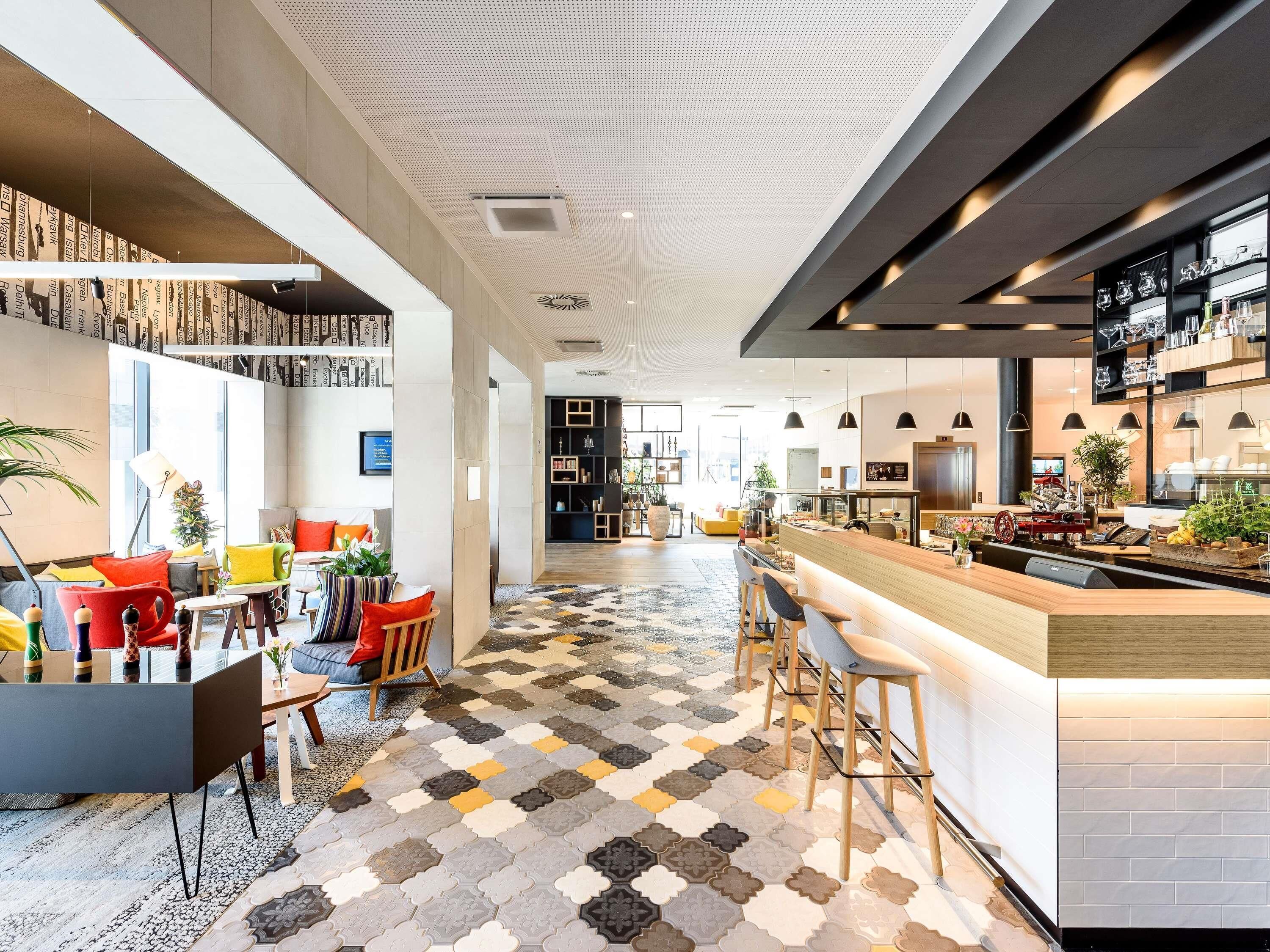 A modern hotel lobby with a central bar area, seating arrangements, and a patterned floor.