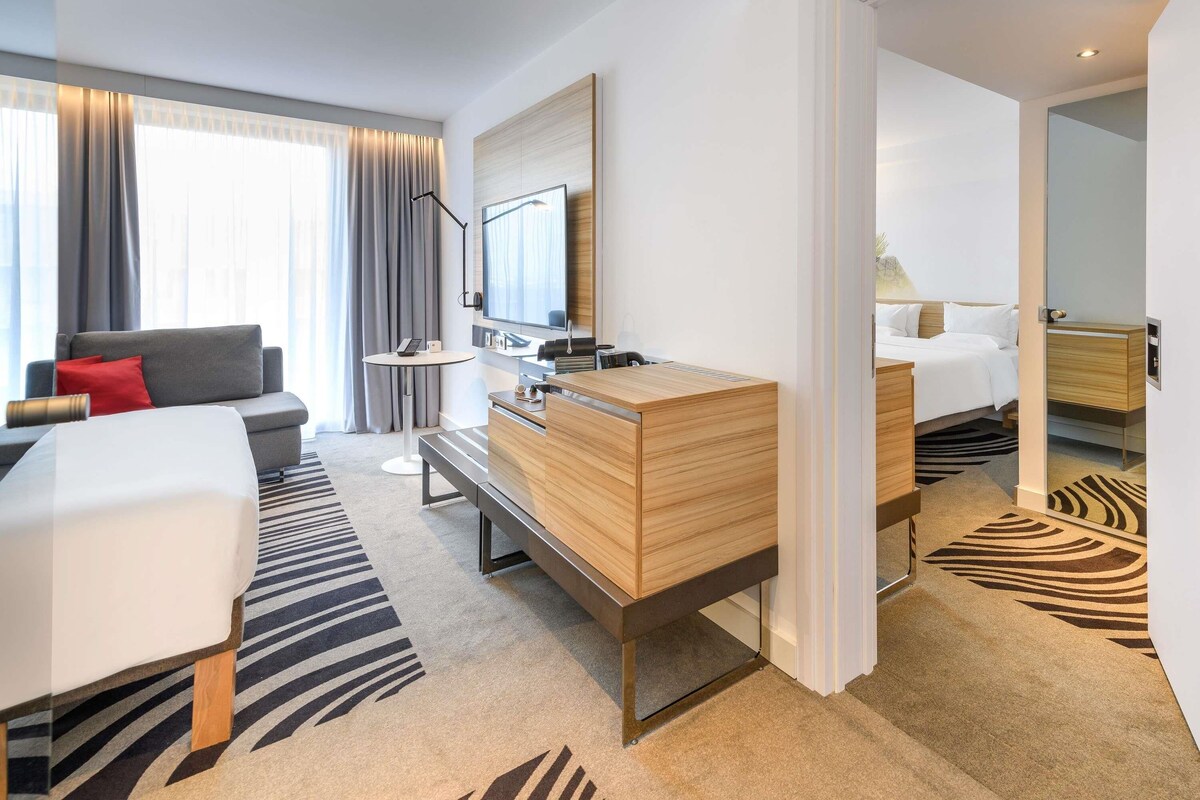 A modern hotel room with a bed, a desk, a sofa, and a large mirror.