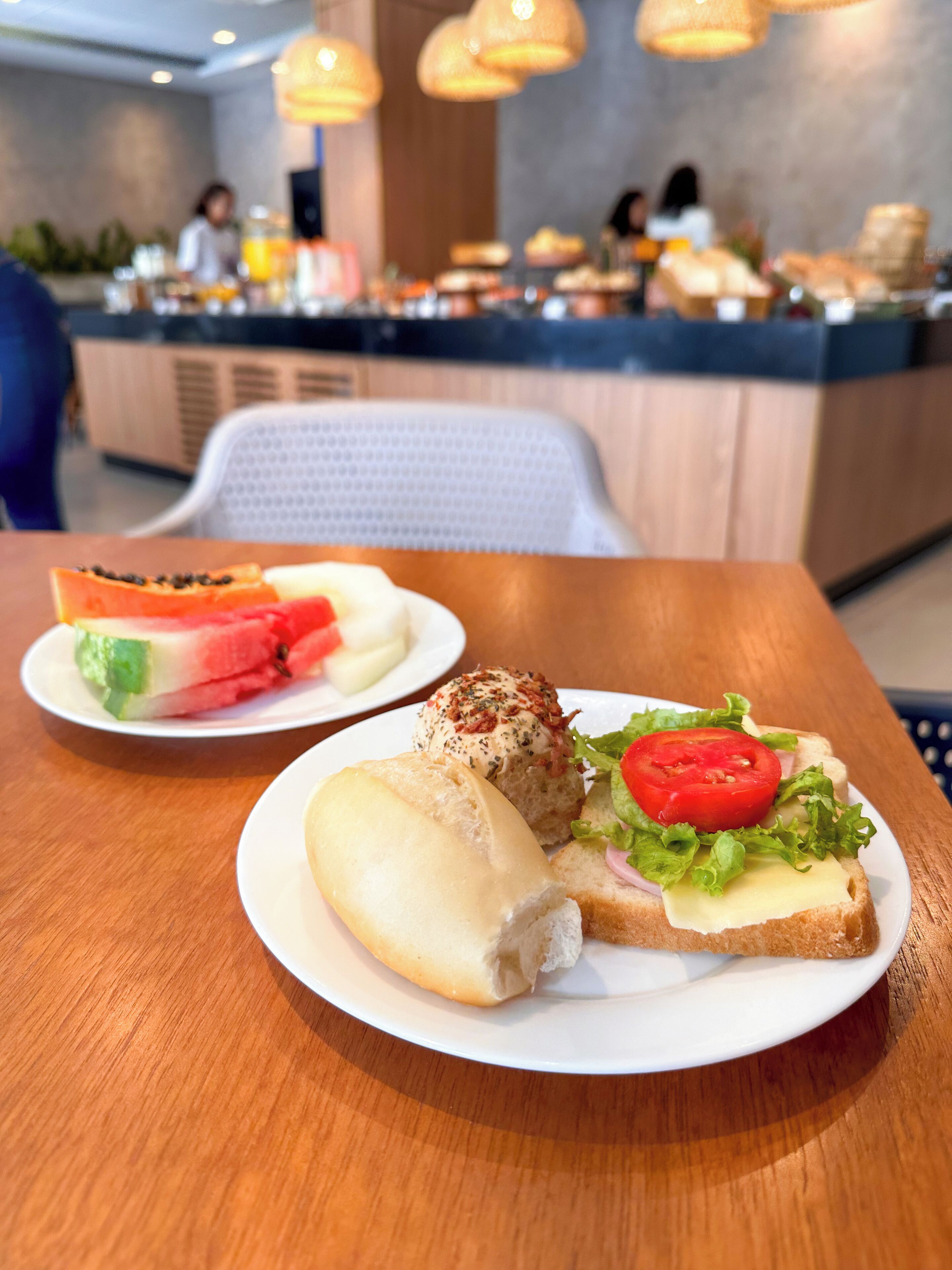 A table with two plates of food, one with a sandwich and the other with a pastry and fruit.