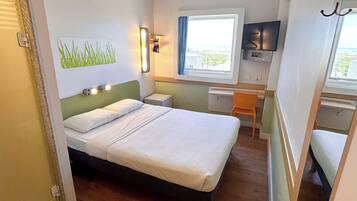 A hotel room with a bed, a desk, a chair, a TV, and a window with a view.
