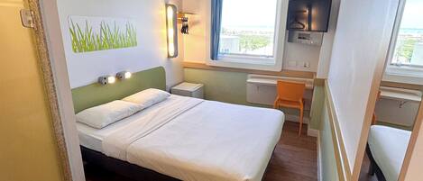 Habitación de hotel con cama, escritorio, silla, televisor y ventana con vistas.
