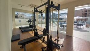 A gym with exercise equipment, a treadmill, and a view of outdoor seating and a pool.