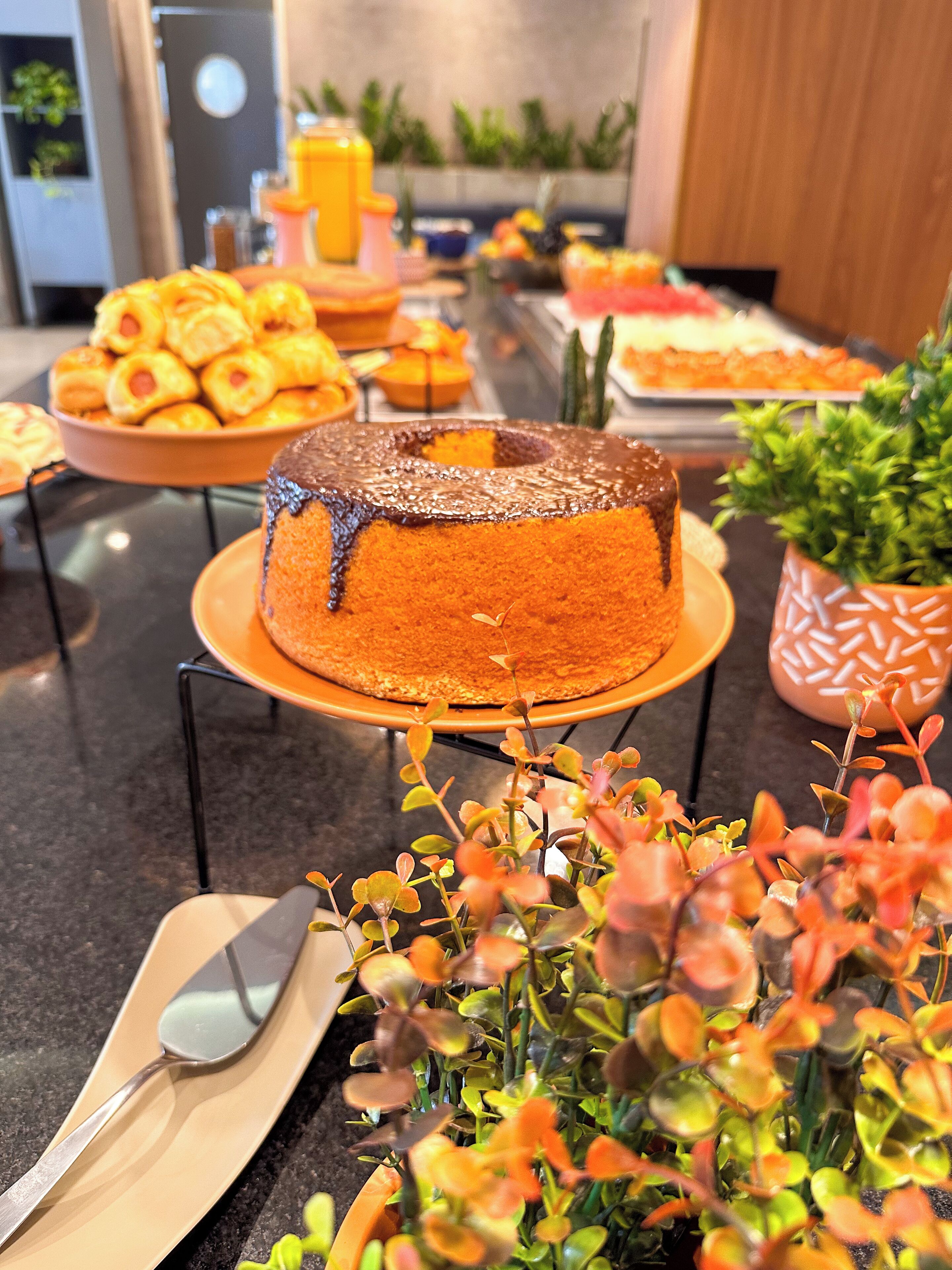 A buffet table with a variety of food items including a bundt cake, pastries, and a plant arrangement.