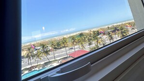 A window view of a beach with palm trees, a pool, and a clear sky.