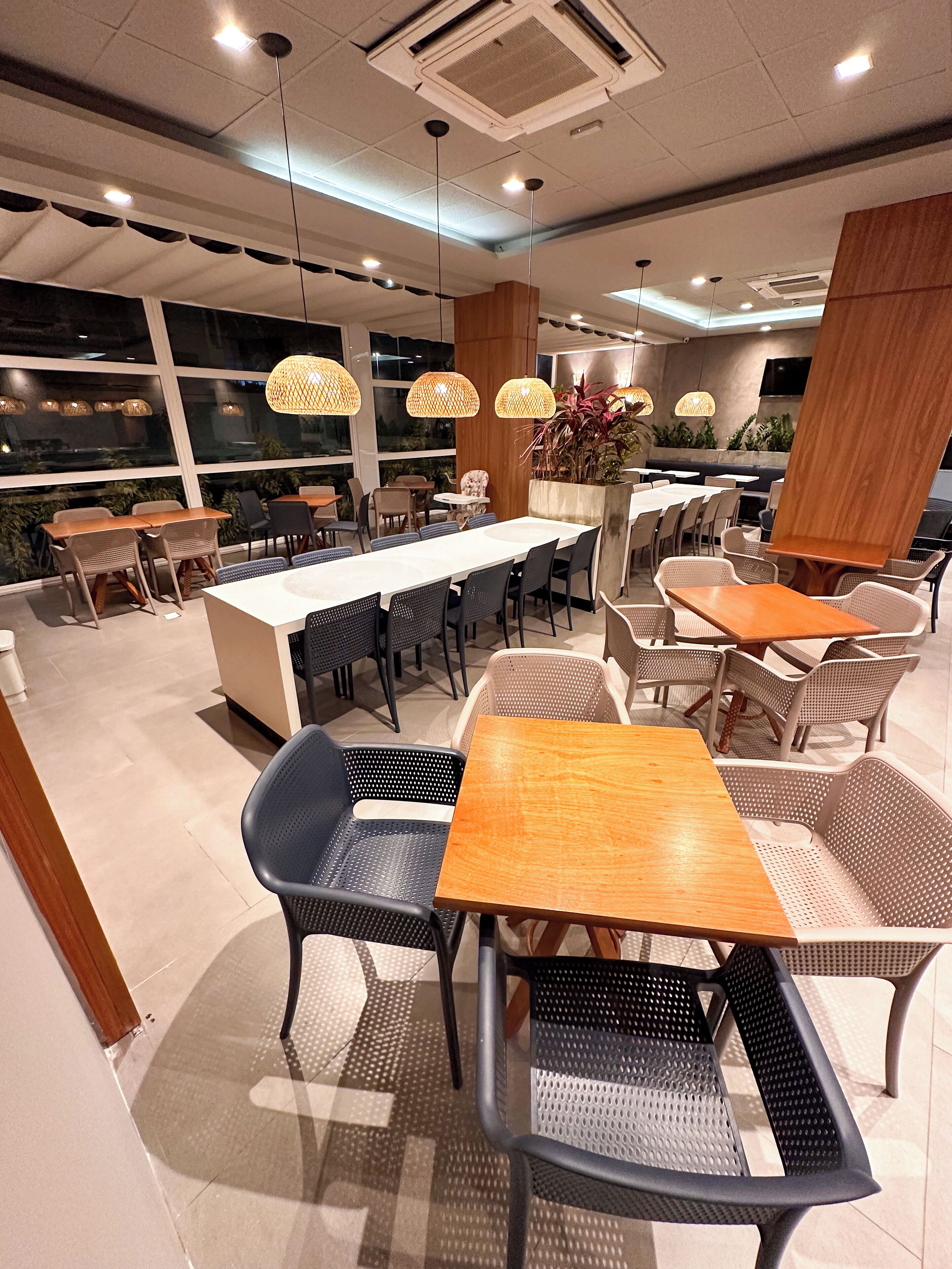 A modern dining area with multiple tables and chairs, large windows, and hanging pendant lights.