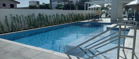 A swimming pool with a metal ladder, surrounded by a low wall and plants.