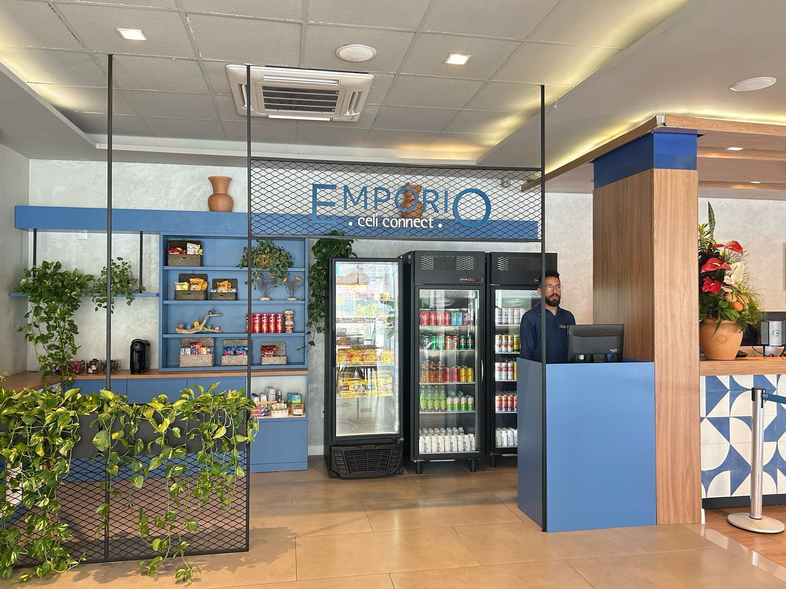 A modern reception area with a blue and white color scheme, featuring a 'Celi connect' sign above a counter, surrounded by shelves stocked with snacks and beverages, and two refrigerators stocked with drinks.