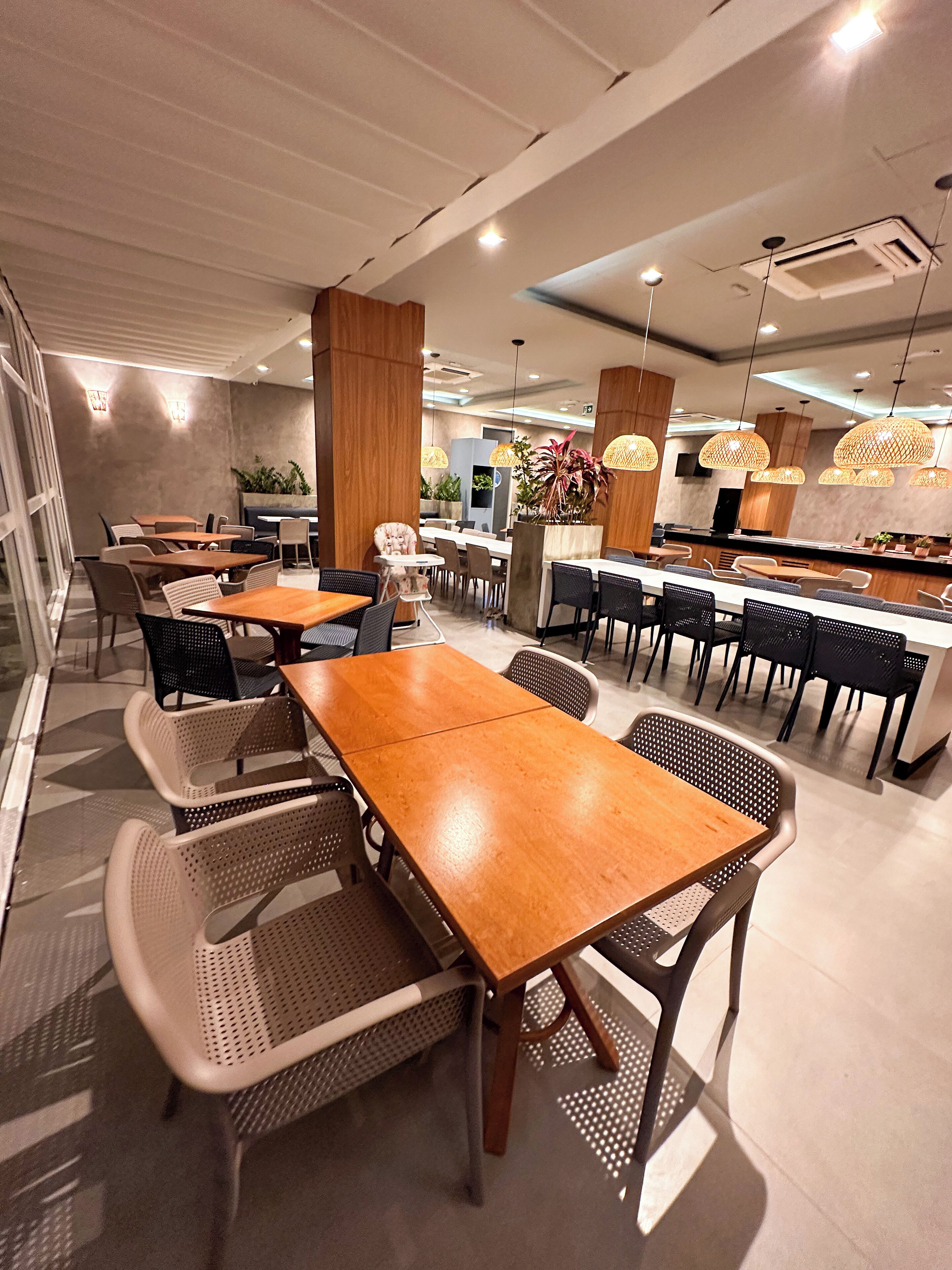 Un interior de restaurante moderno con mesas y sillas de madera, iluminación colgante y una zona de bar central.
