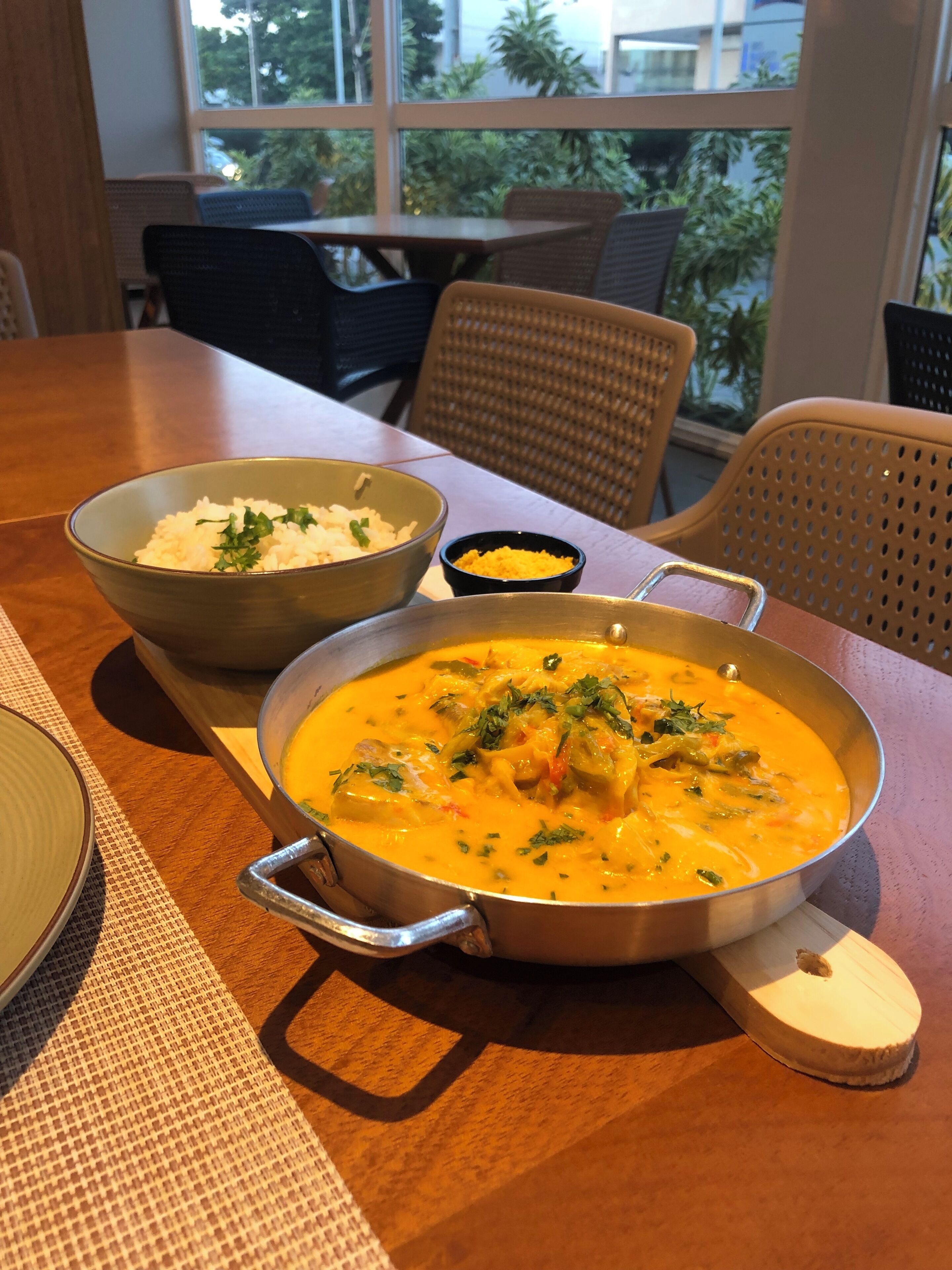 Uma mesa de jantar com um prato de arroz, um prato de curry amarelo e um pequeno recipiente com molho amarelo.
