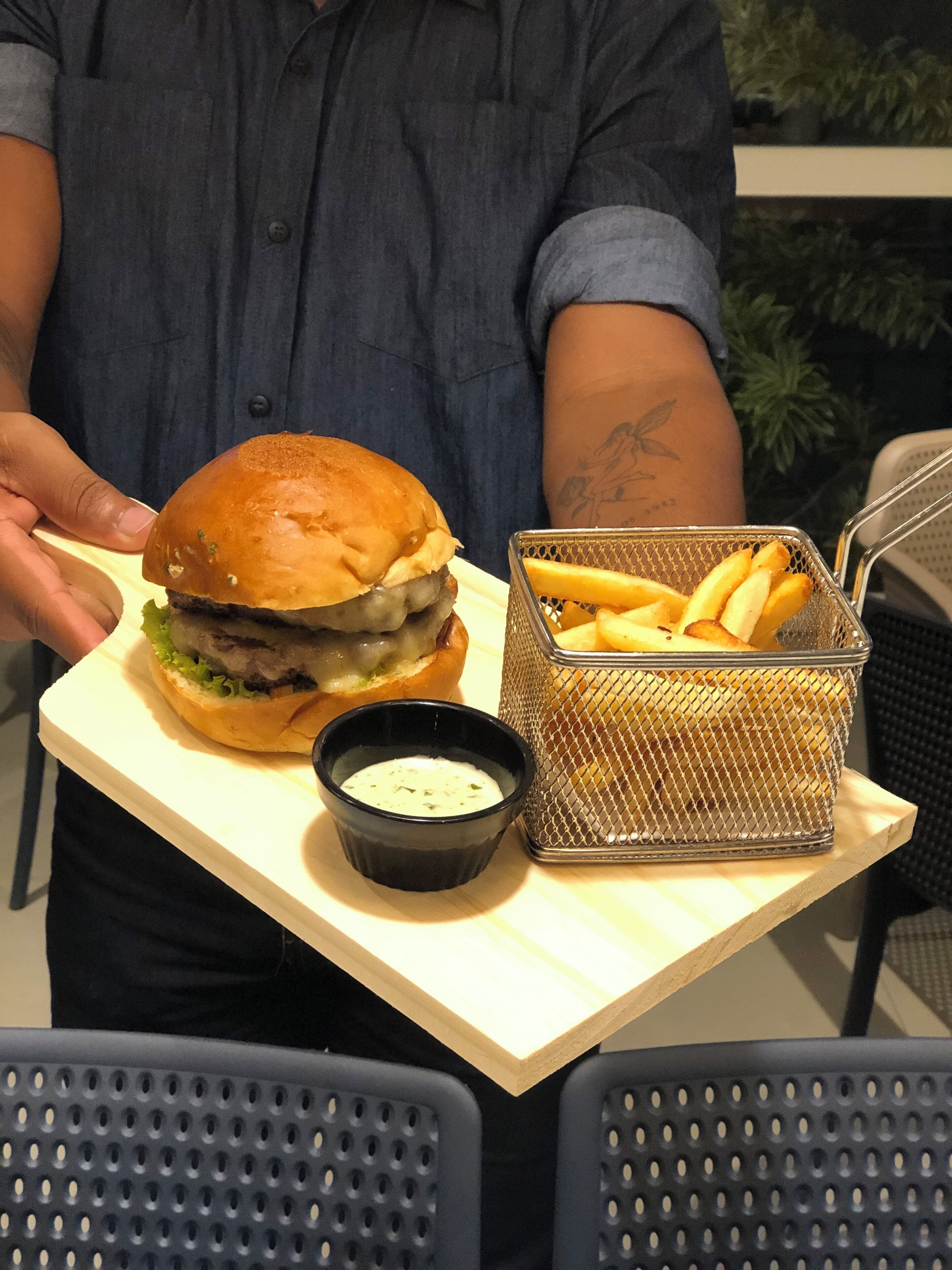 A person holding a tray with a burger, fries, and a small bowl of sauce.