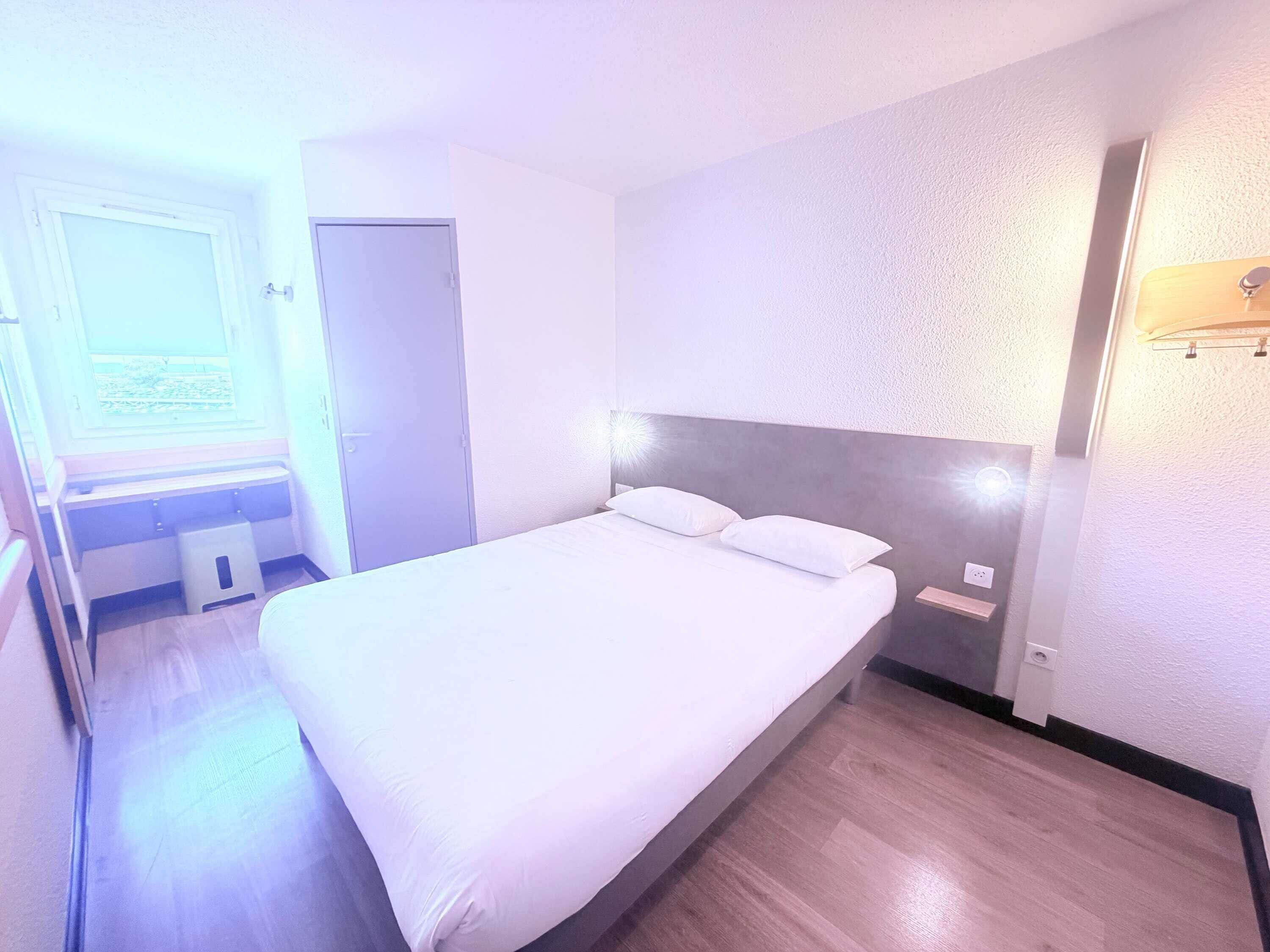 A hotel room with a large bed, a bedside table, a wardrobe, and a window with a view.