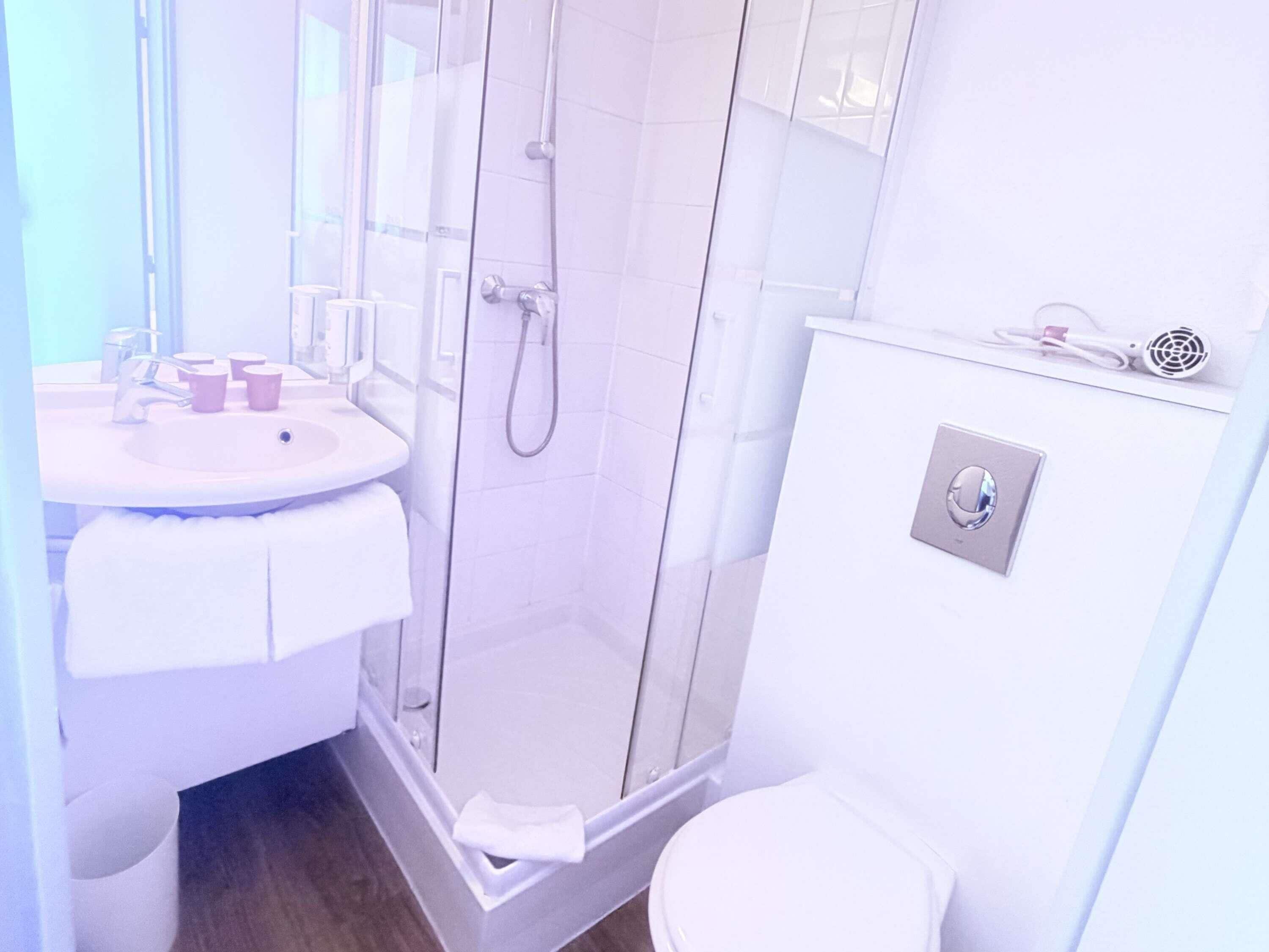 A modern bathroom with a glass-enclosed shower, a white sink with two cups, and a toilet with a bidet attachment.
