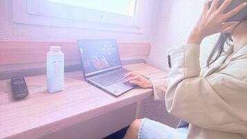 A person using a laptop on a wooden desk with a bottle of water and a remote control beside it.
