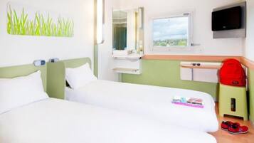 Habitación de hotel con dos camas, un ventanal pequeño, un televisor y una mochila roja sobre un taburete.