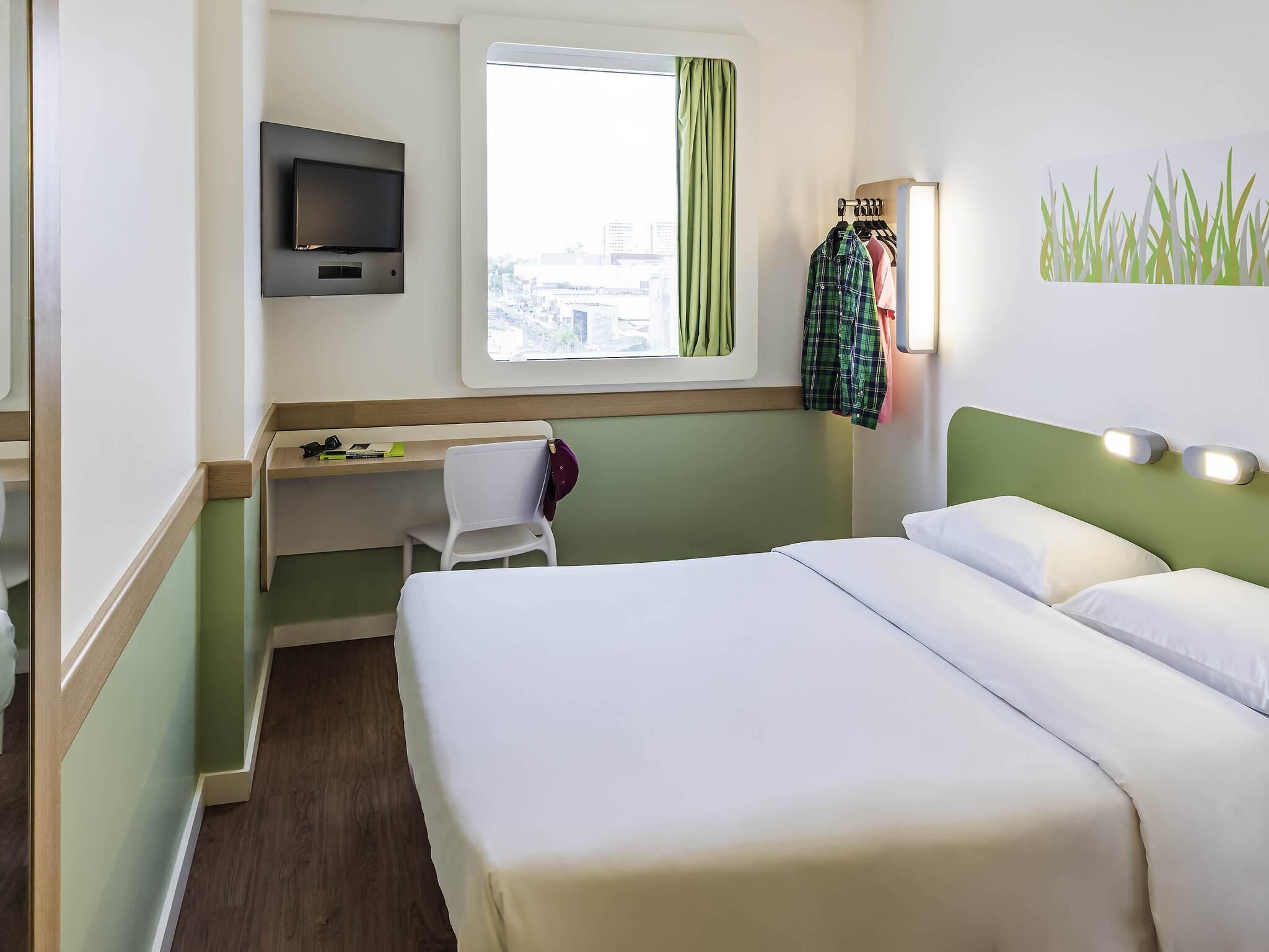 Une chambre d’hôtel avec un lit, un bureau, une chaise, une télévision et une fenêtre avec des rideaux.