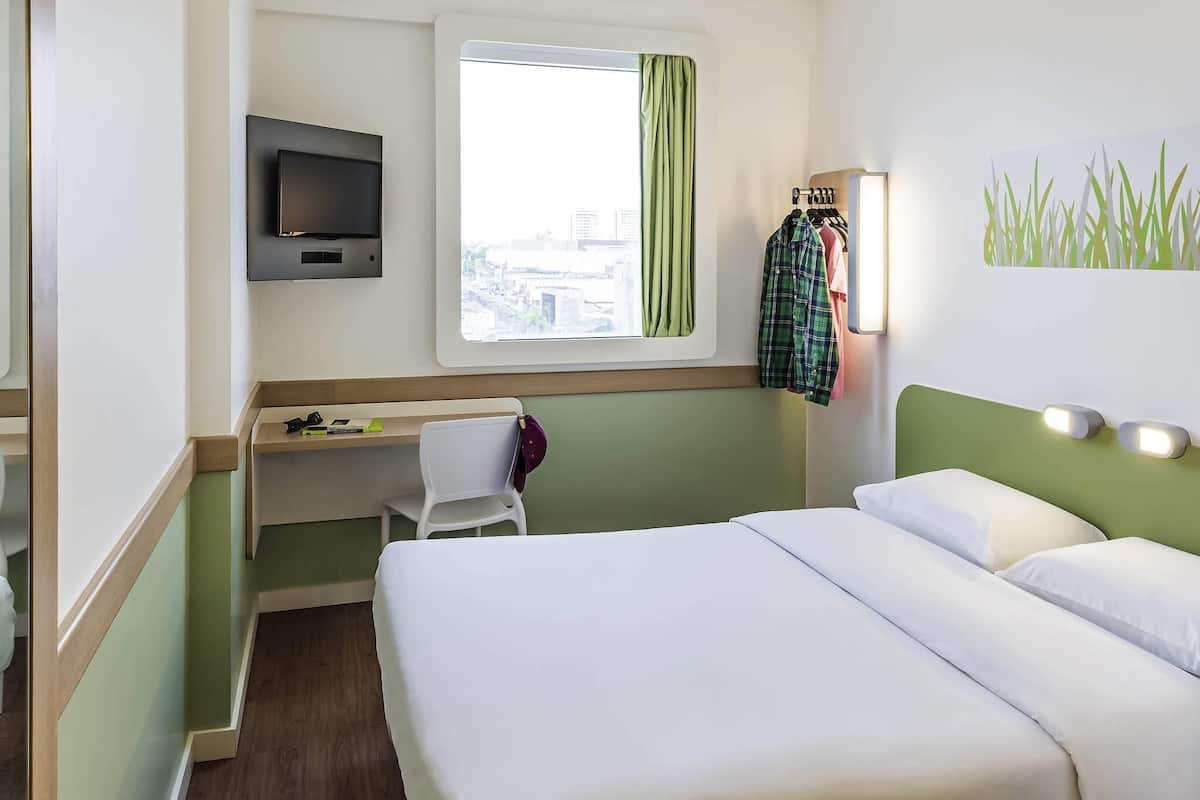 Ein Hotelzimmer mit Bett, Schreibtisch, Stuhl, Fernseher und einem Fenster mit Vorhängen.